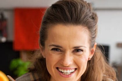 Happy young woman eating pumpkin soup in kitchen