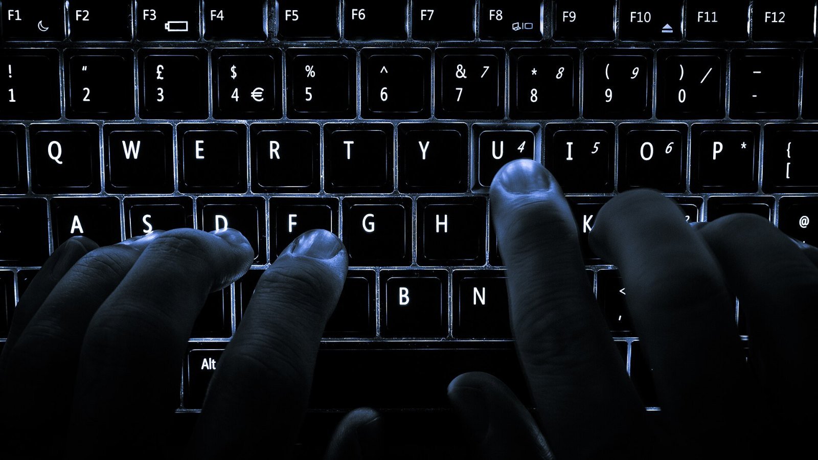Hands typing on a backlit laptop keyboard in the dark