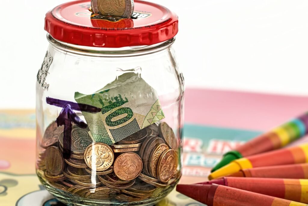Glass savings jar filled with coins and a folded dollar bill next to crayons