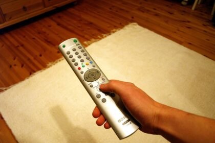 A hand holding a TV remote control in front of a television