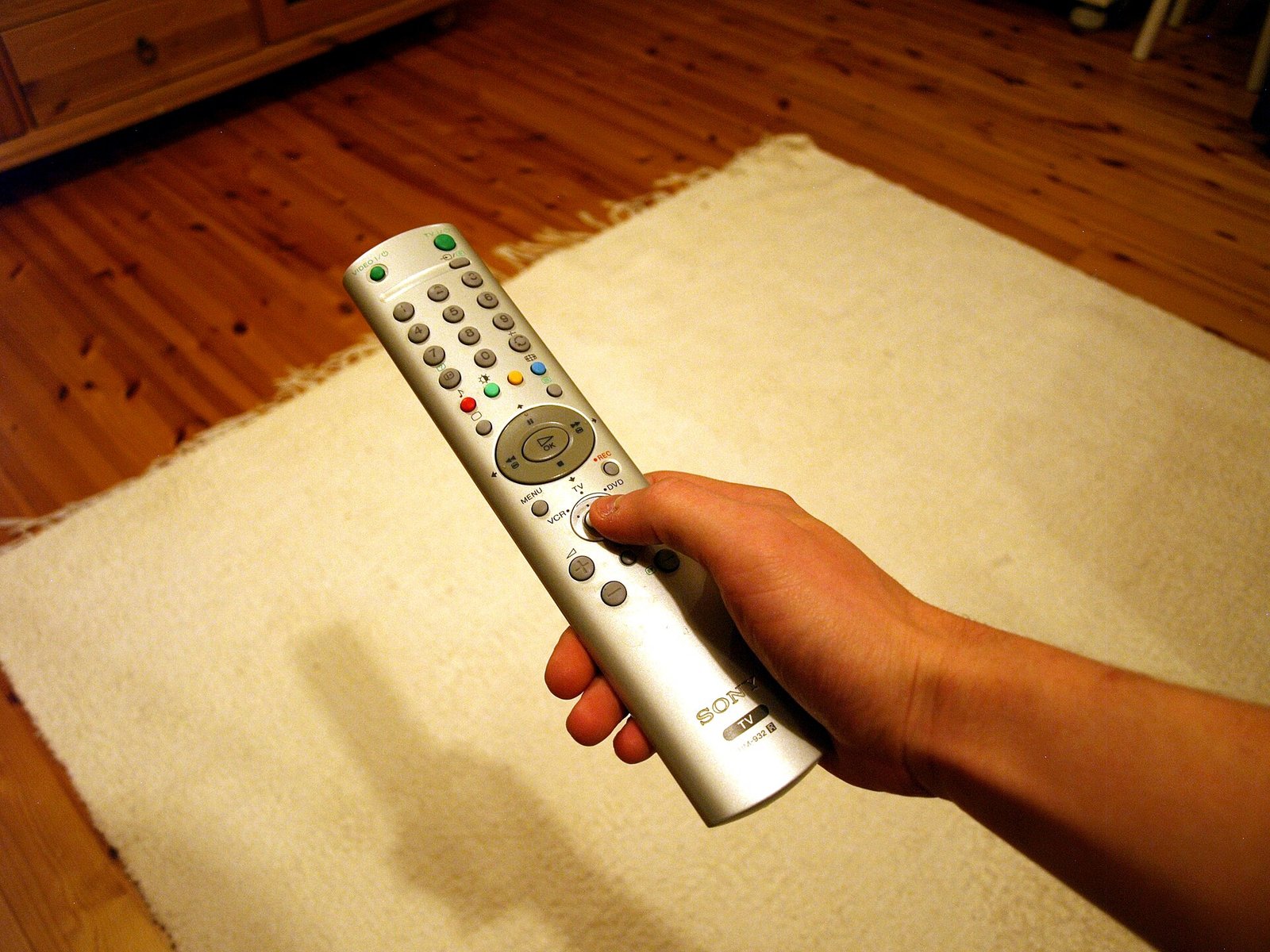 A hand holding a TV remote control in front of a television